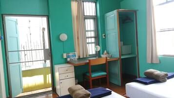 A room with teal walls, a desk with a chair, a wardrobe, a bed with two pillows, and a window with curtains.