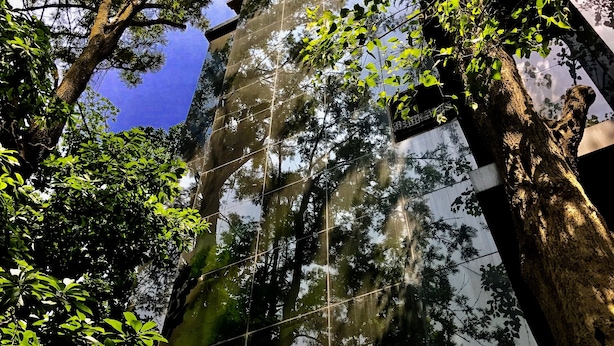 Un edificio alto con facciata in vetro che riflette alberi e cielo circostanti.