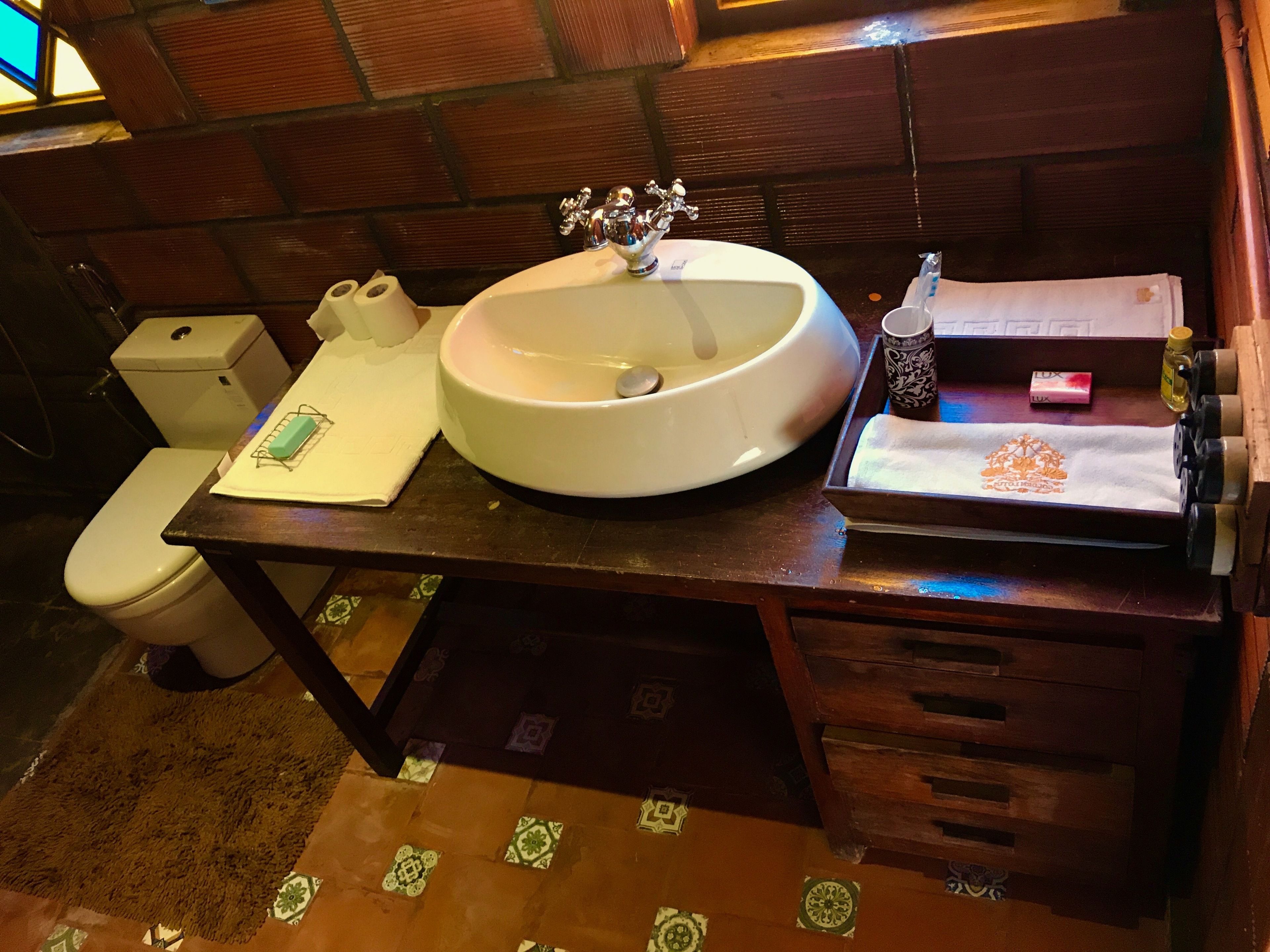 A bathroom with a sink, toilet, and a small table with toiletries.