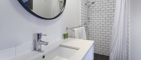 Un baño con un lavamanos blanco, un espejo y una zona de ducha con cortina blanca.