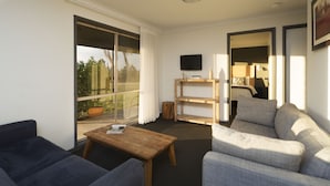 A modern living room with a sofa, a coffee table, and a TV mounted on the wall. - Harkham Lodge (Pokolbin)