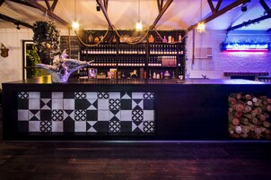 Zona de bar con suelo de baldosas de diseño a cuadros, vigas de madera, luces colgantes y una estantería para vinos.