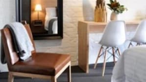 A hotel room with a large mirror, a bedside table with a lamp, a chair, and a bed. - Harkham Lodge (Pokolbin)