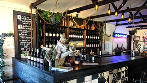 A bar area with a wooden counter, black and white patterned tiles, and a rustic decor including a large animal sculpture. - Harkham Lodge (Pokolbin)