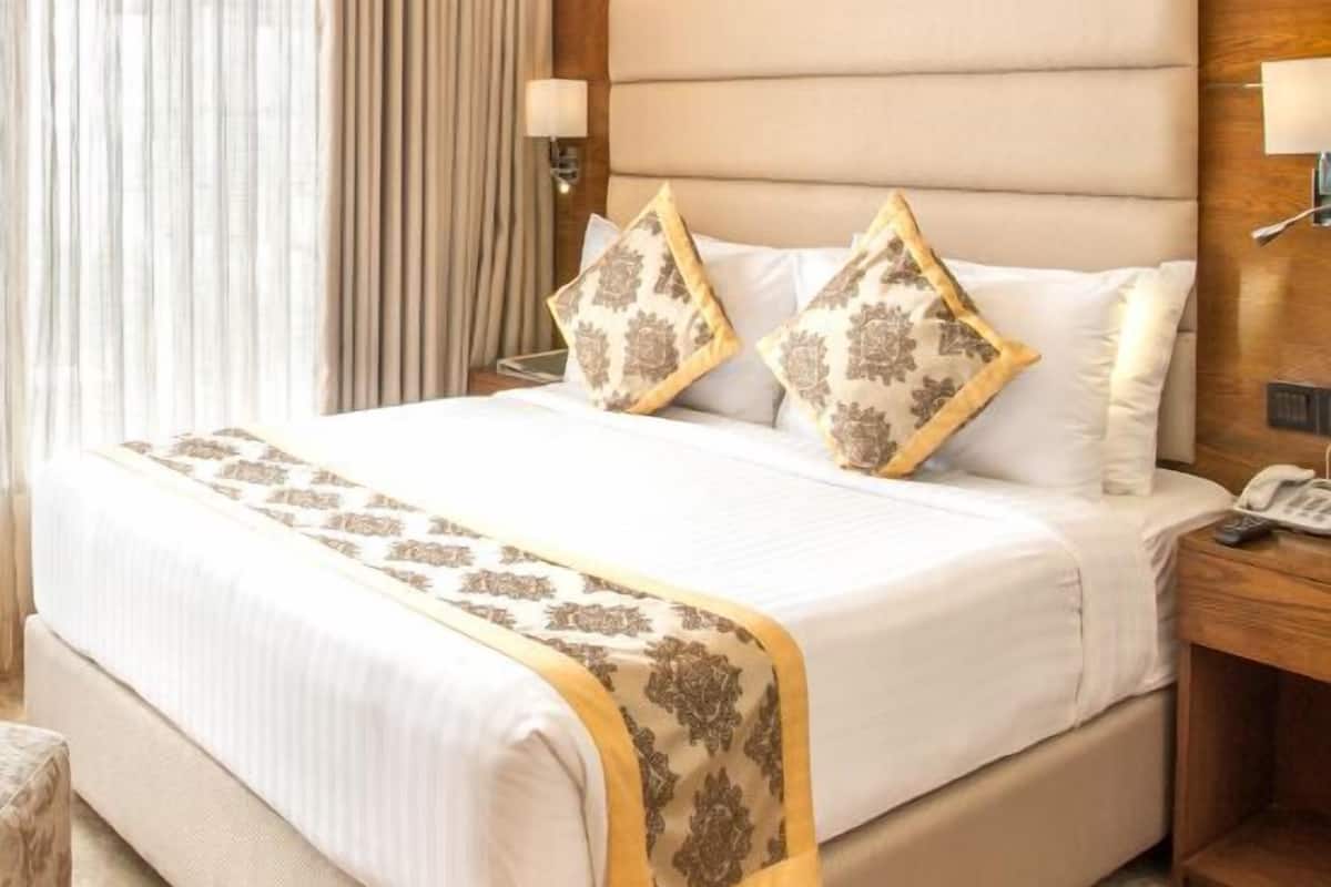Hotelkamer met een groot bed, een houten hoofdeinde, een nachtkastje met lamp en een raam met gordijnen.