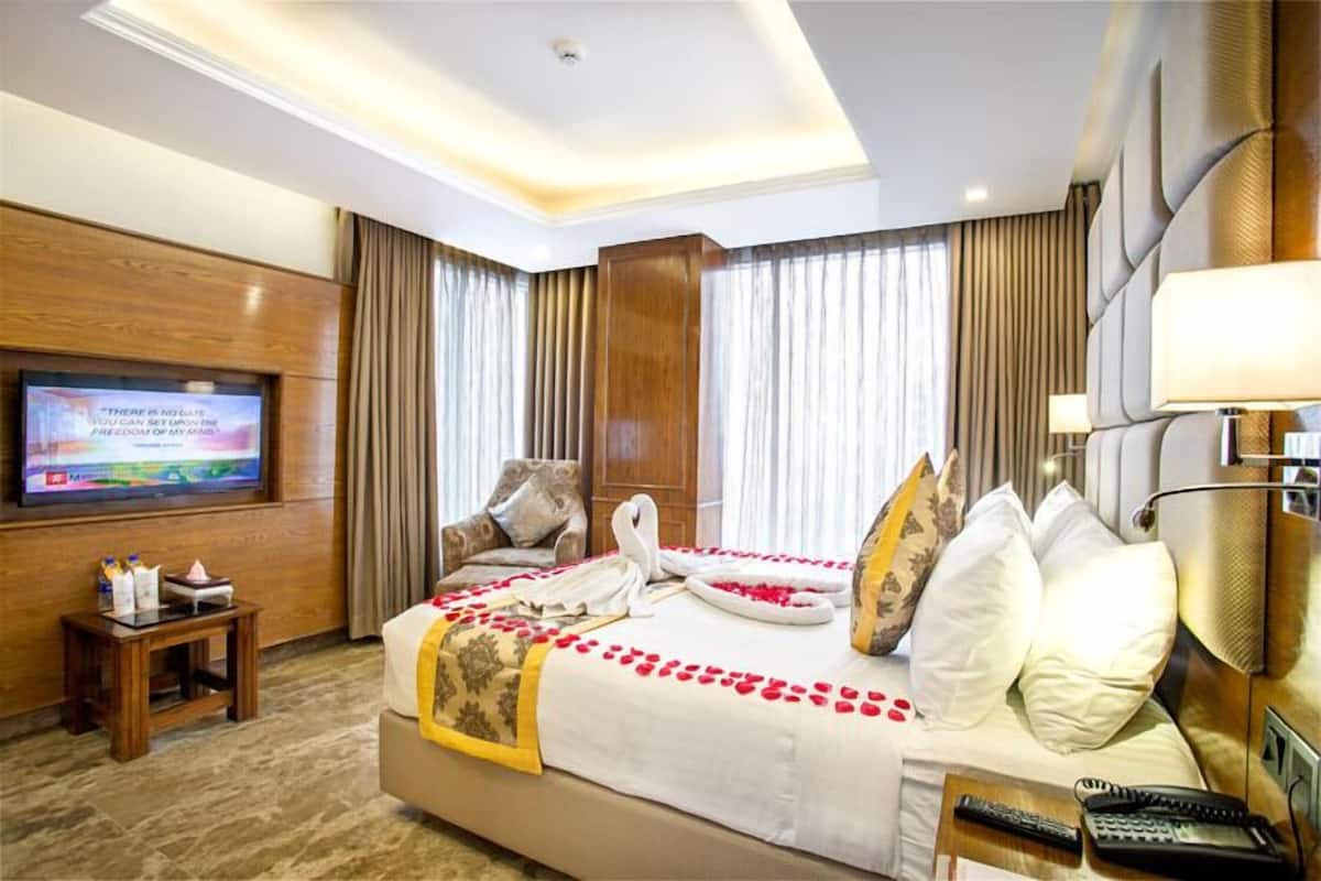 Een hotelkamer met een groot bed, een televisie aan de muur, een klein tafeltje en een bedlampje.
