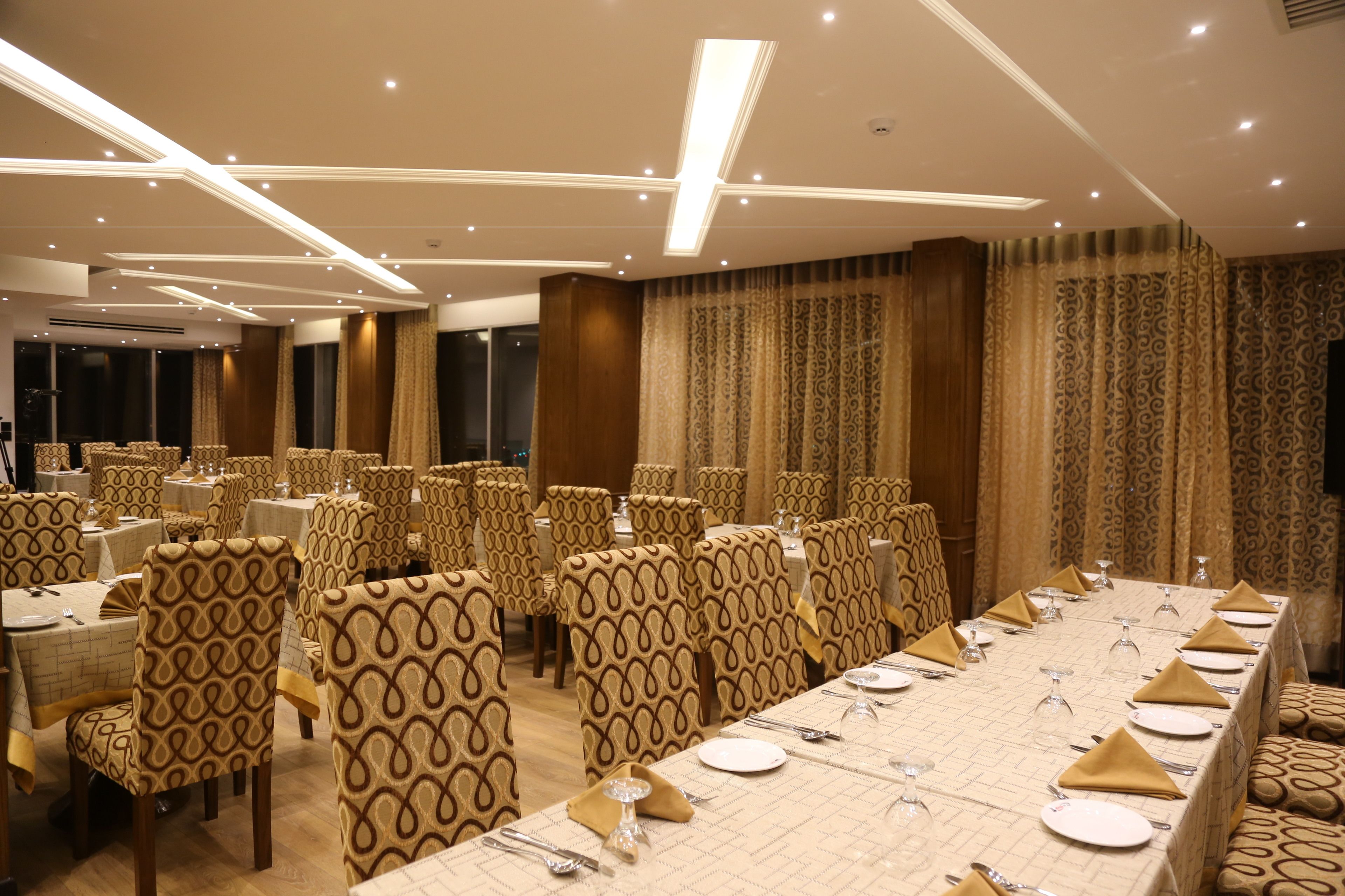 Un salón de banquetes con varias mesas redondas dispuestas para comer, cada una con sillas y completa con loza.