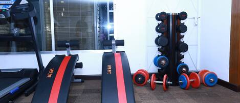 Un gimnasio con cintas de correr, bancos de pesas y un estante con mancuernas.