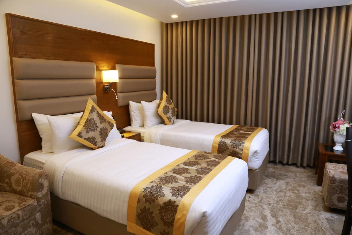 Een hotelkamer met twee bedden, een houten hoofdeinde, een nachtkastje met een lamp, een bank en een gordijn.