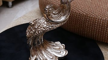 Une statue décorative représentant un paon en argent, posée sur un socle circulaire noir.