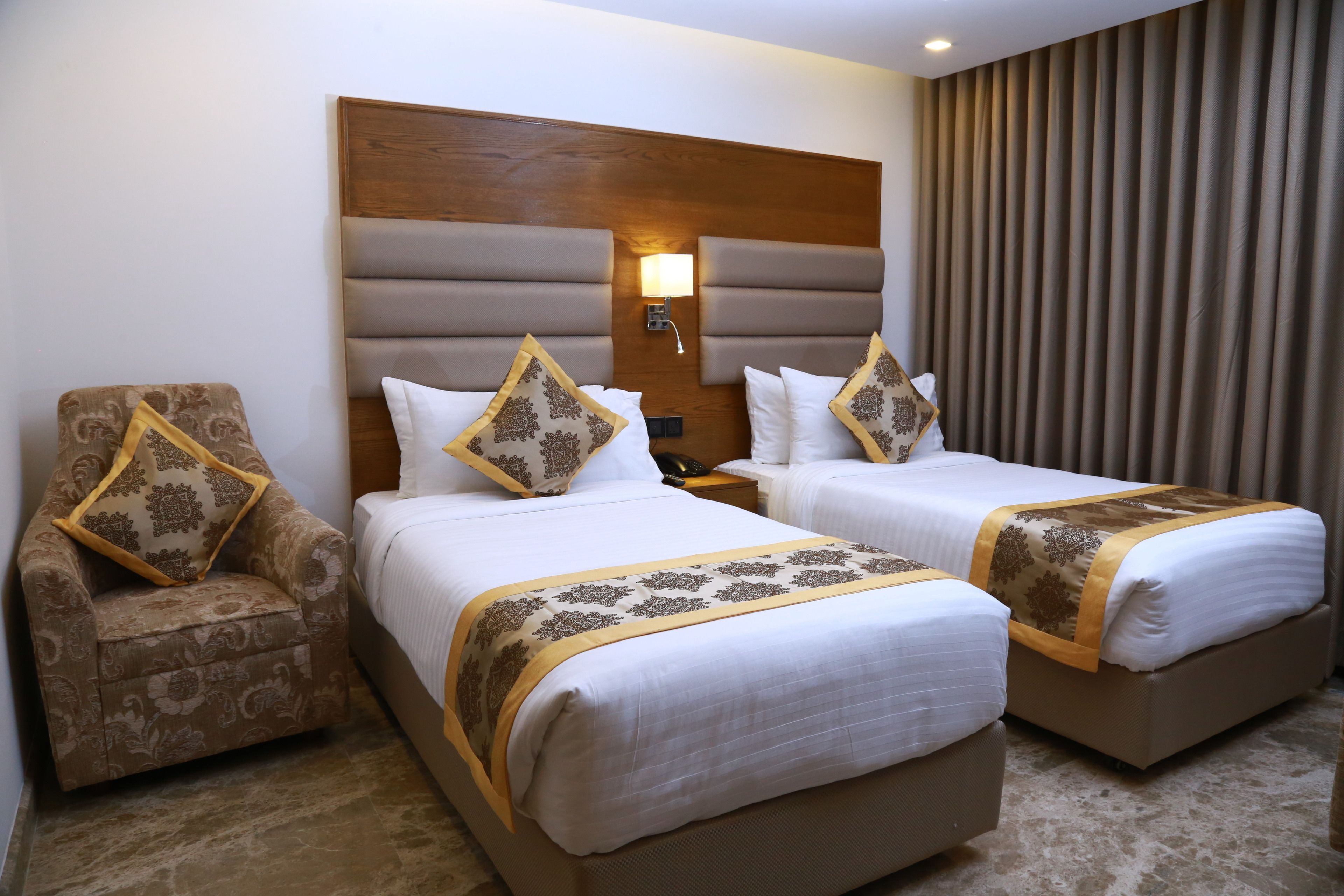A hotel room with two beds, a wooden headboard, a nightstand, a lamp, and a chair.