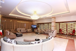 A spacious living room with a large round sofa, multiple armchairs, a coffee table, and a television.