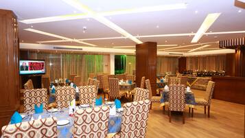 A restaurant with patterned chairs and tables, a TV screen, and a bar area.