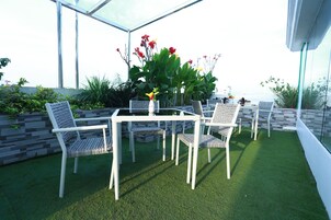 Una terraza en la azotea con techo de vidrio, mobiliario blanco y césped artificial.