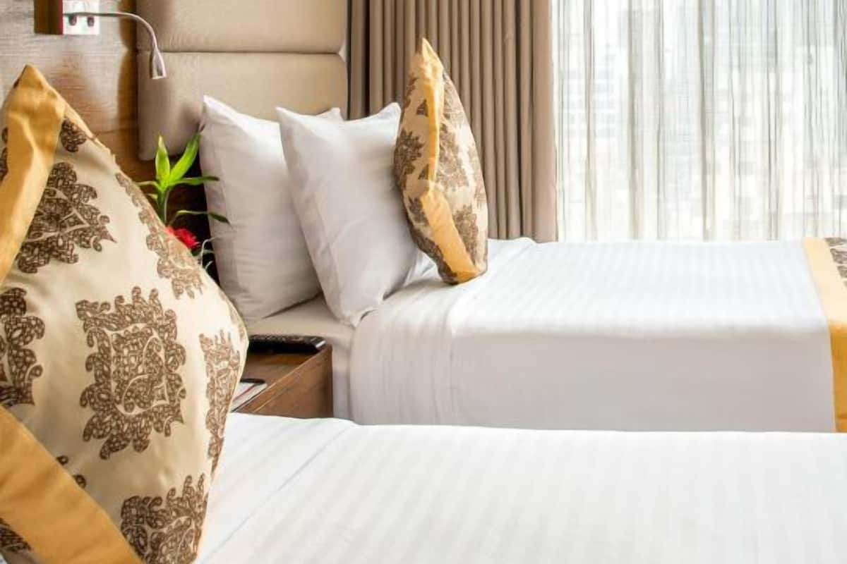 Een hotelkamer met een bed, nachtkastje, lamp en een raam met gordijnen.