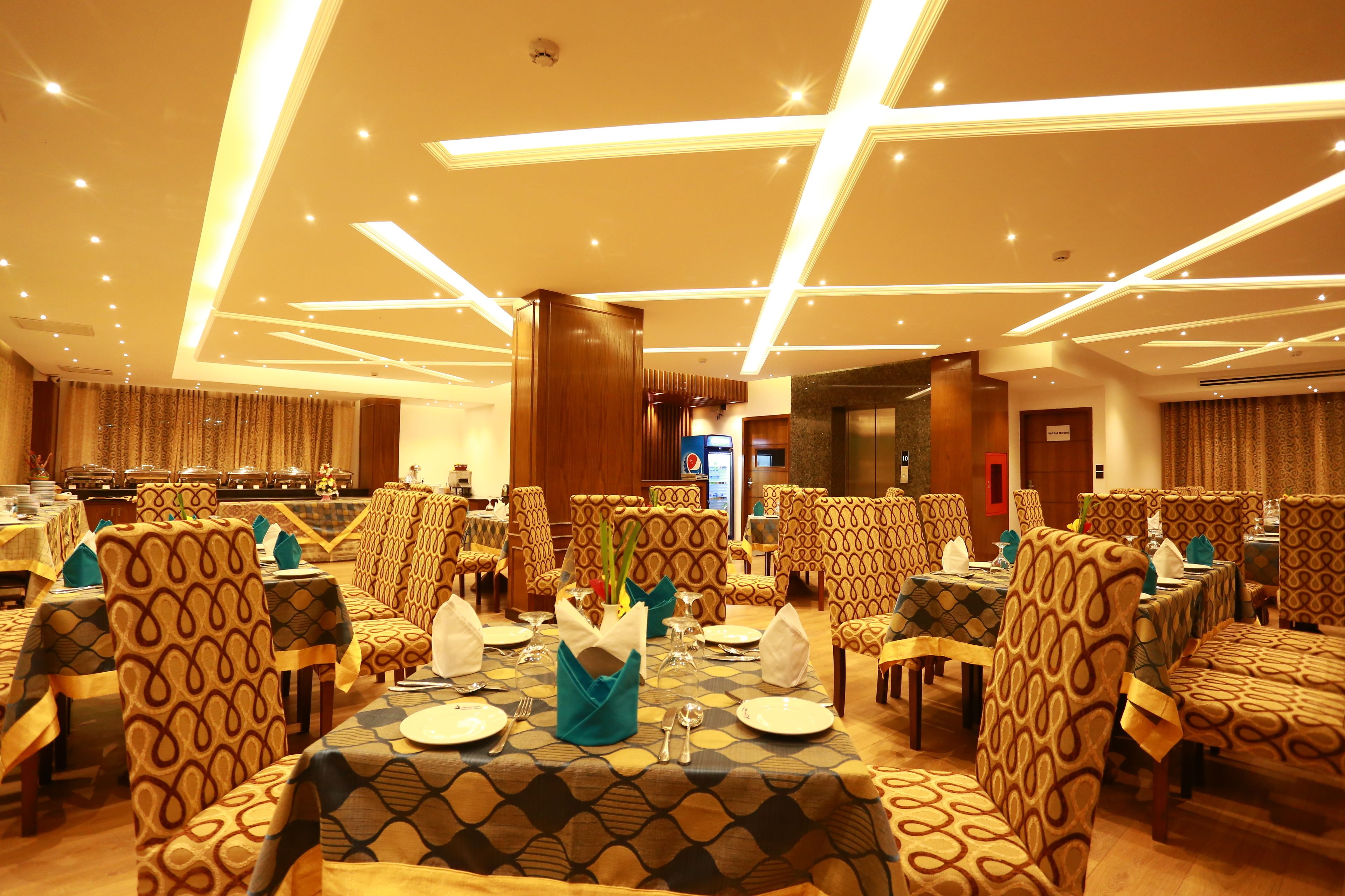 A dining area with tables set for four, patterned chairs, and a modern ceiling design.