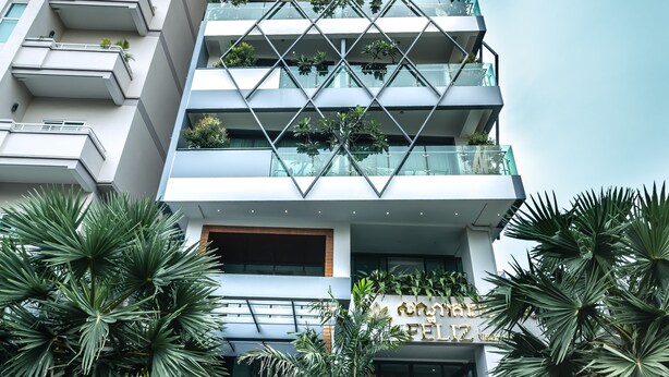 A modern high-rise building with multiple balconies, a central atrium, and lush greenery. - Feliz Urban Hotel (Phnom Penh)