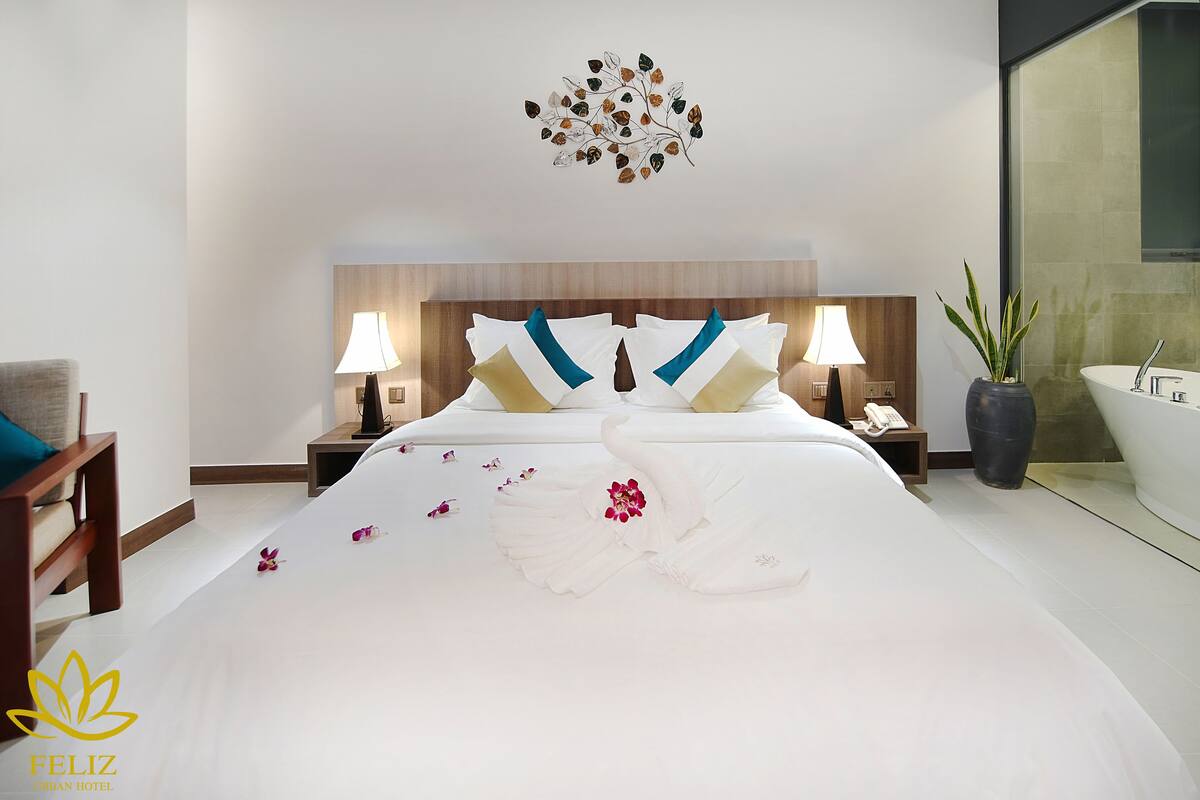 A hotel room with a neatly made bed, two bedside lamps, a potted plant, and a view of the bathroom.