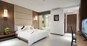 A modern hotel room with a large bed, bedside table, potted plant, and a television. - Feliz Urban Hotel (Phnom Penh)