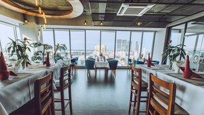 A modern dining area with high ceilings, large windows, and a view of the cityscape. - Feliz Urban Hotel (Phnom Penh)