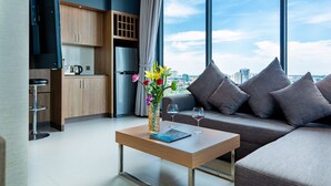 A modern living room with a sofa, a coffee table with a vase of flowers, and a view of the city through large windows. - Feliz Urban Hotel (Phnom Penh)