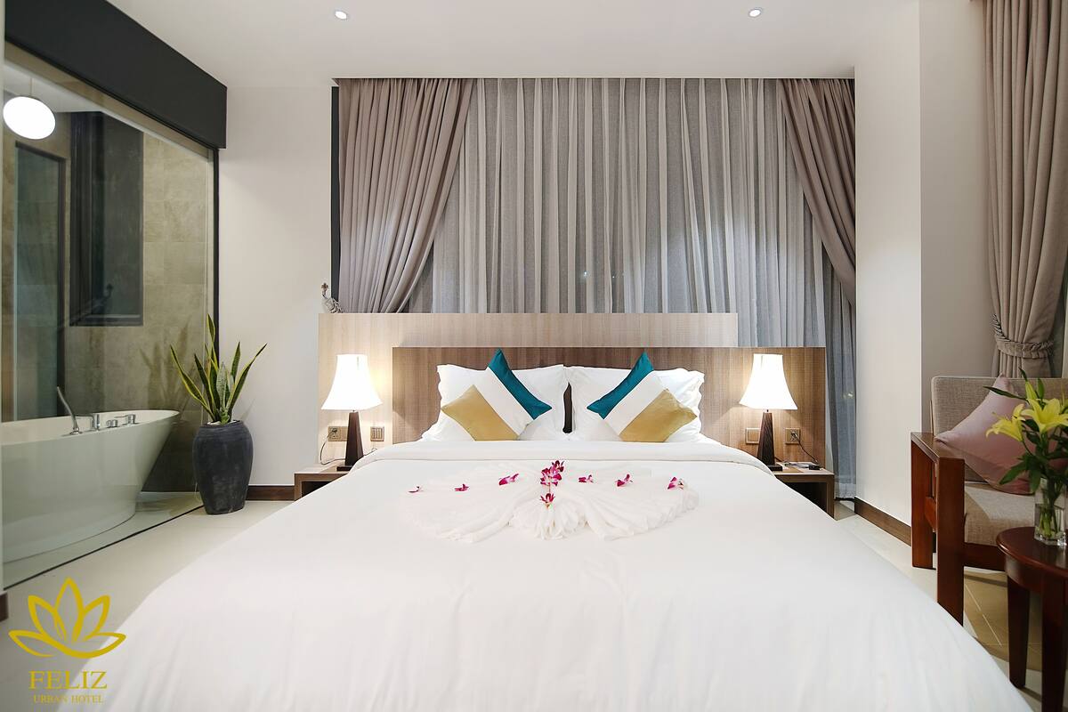 A hotel room with a large bed, a bathroom with a bathtub, and a nightstand with a lamp.