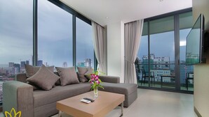 A modern living room with a grey sofa, a wooden coffee table, and a vase with flowers. - Feliz Urban Hotel (Phnom Penh)