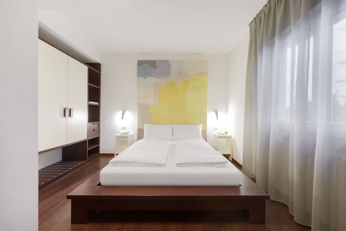 Una habitación de hotel con una cama grande, suelo de madera, un armario y un cuadro en la pared.