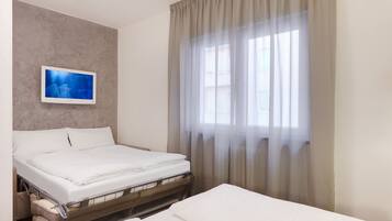 A hotel room with a bed, a television mounted on the wall, and a window with curtains.