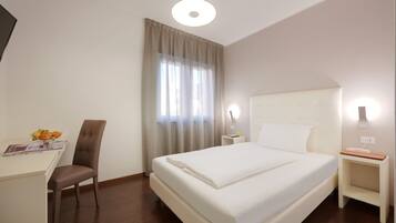 Ein Hotelzimmer mit einem Bett, einem Schreibtisch, einem Stuhl, einem Nachttisch und einem Vorhangfenster.