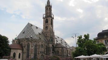 Una iglesia histórica con una torre alta y una fachada detallada, rodeada por una plaza pública con gente y mesas al aire libre.