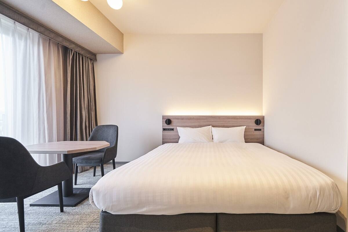A hotel room with a bed, a desk, a chair, and a window with curtains.