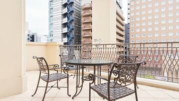 A balcony with a glass table and four metal chairs, surrounded by a metal railing.
