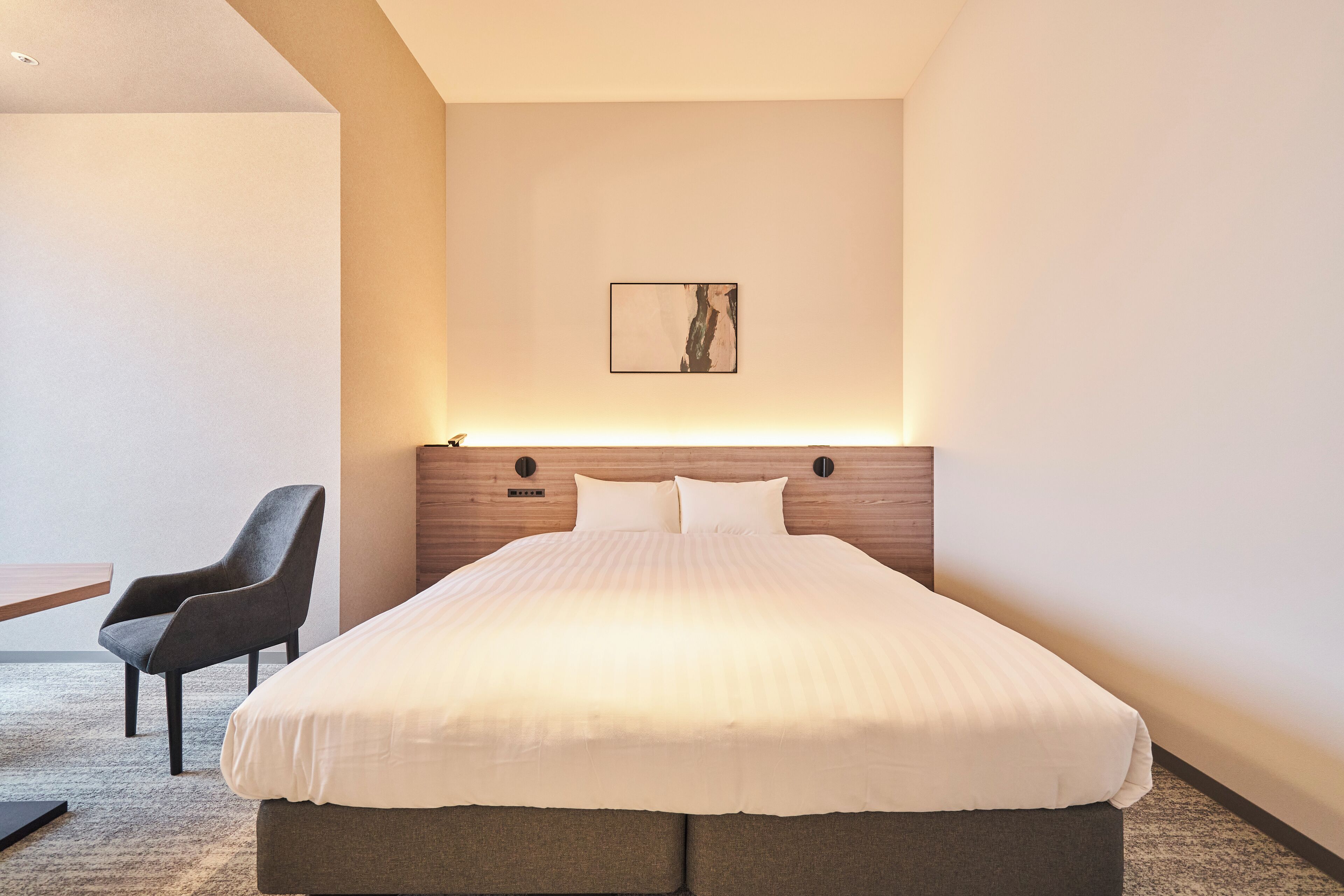 A modern hotel room with a large bed, a chair, and a small table.