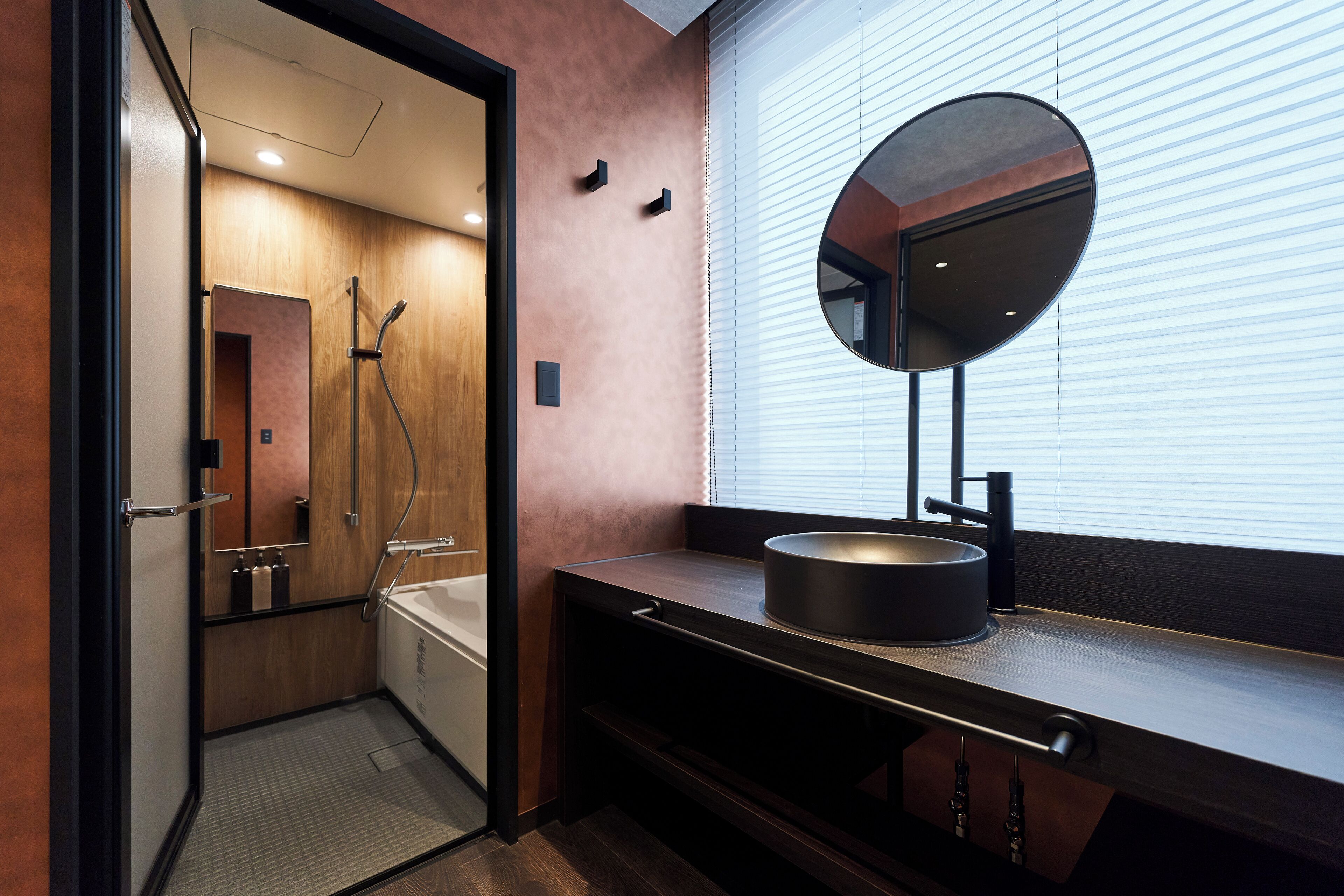 A modern bathroom with a walk-in shower, a round mirror, and a dark countertop with a sink.