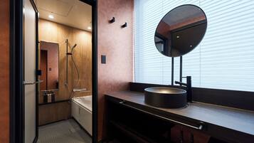 A modern bathroom with a walk-in shower, a round mirror, and a dark countertop with a sink.