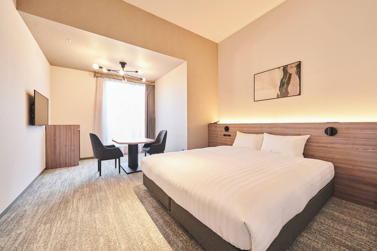 A hotel room with a large bed, a desk with two chairs, a flat-screen TV, and a painting on the wall.