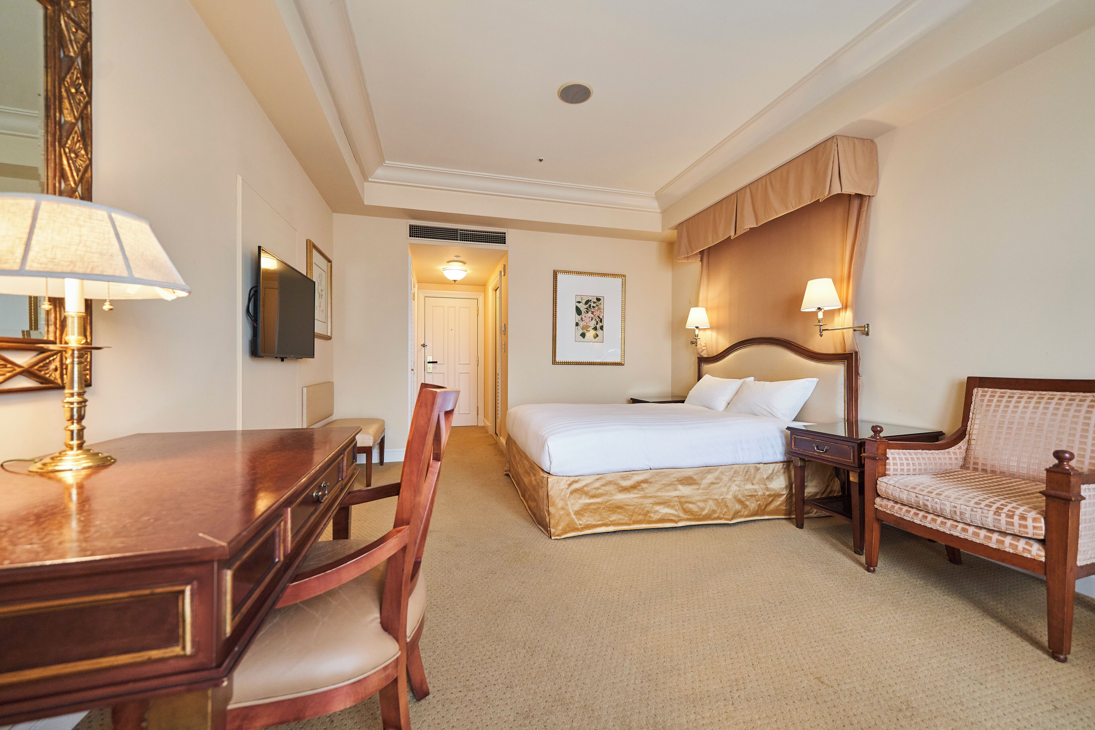 Een hotelkamer met een bed, bureau, stoel en een grote spiegel.