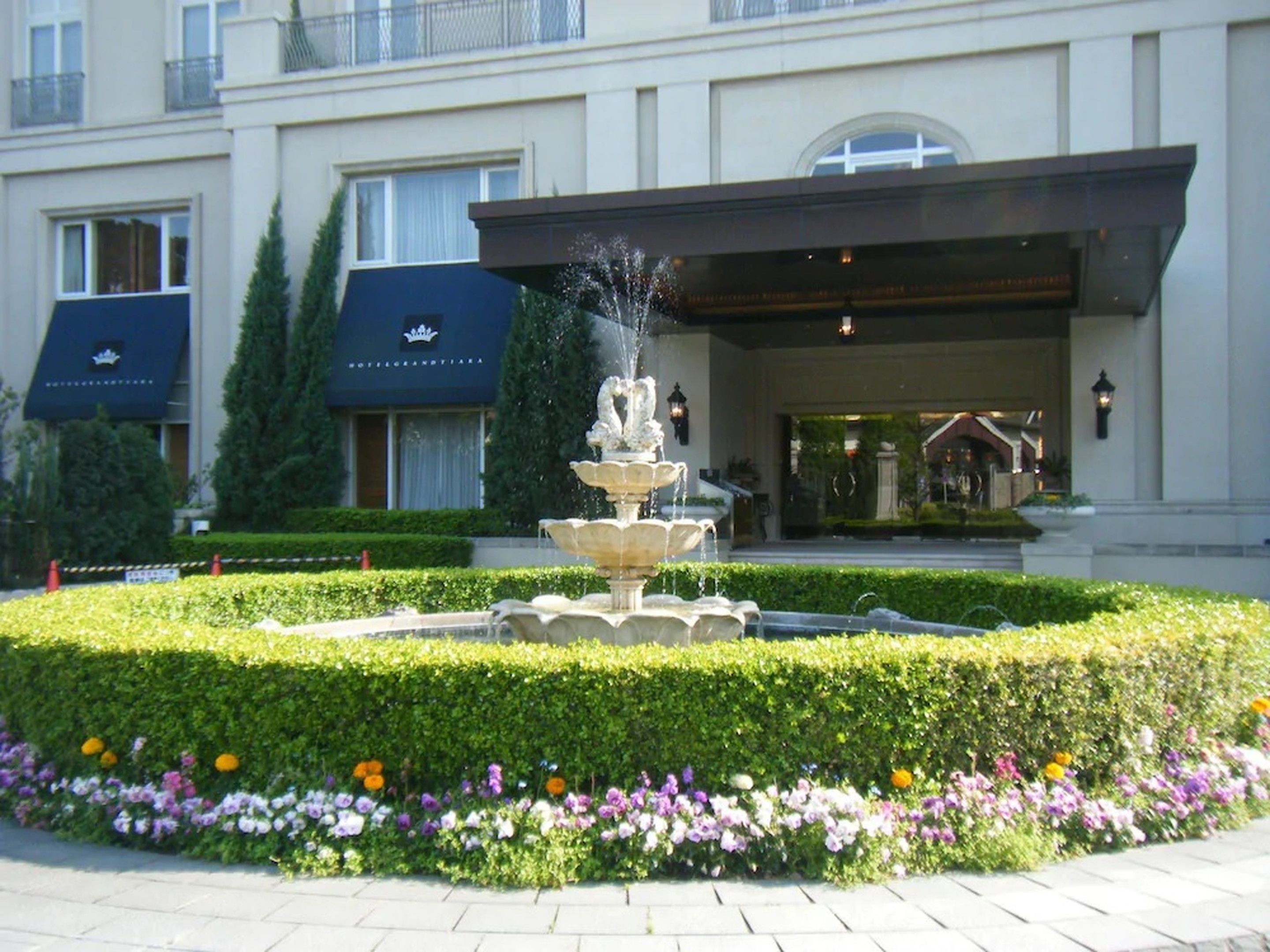 A hotel entrance with a fountain, manicured garden, and a well-maintained hedge.