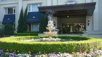 A hotel entrance with a fountain, manicured garden, and a well-maintained hedge.