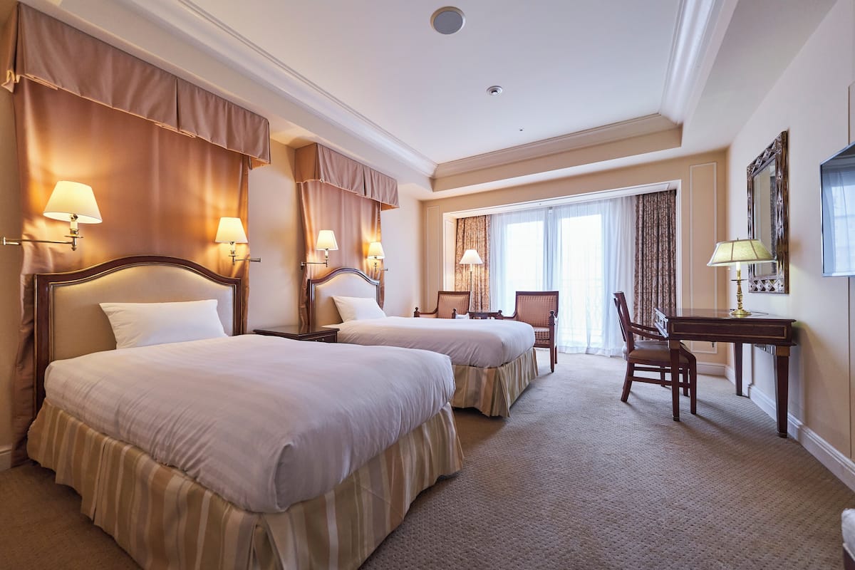 A hotel room with two beds, a desk, and a chair.