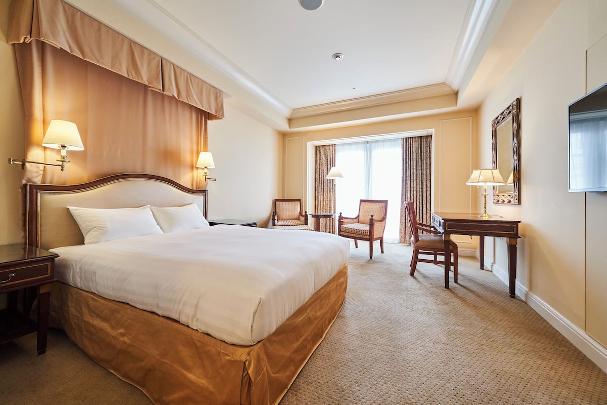 A hotel room with a large bed, two chairs, a desk, and a TV.
