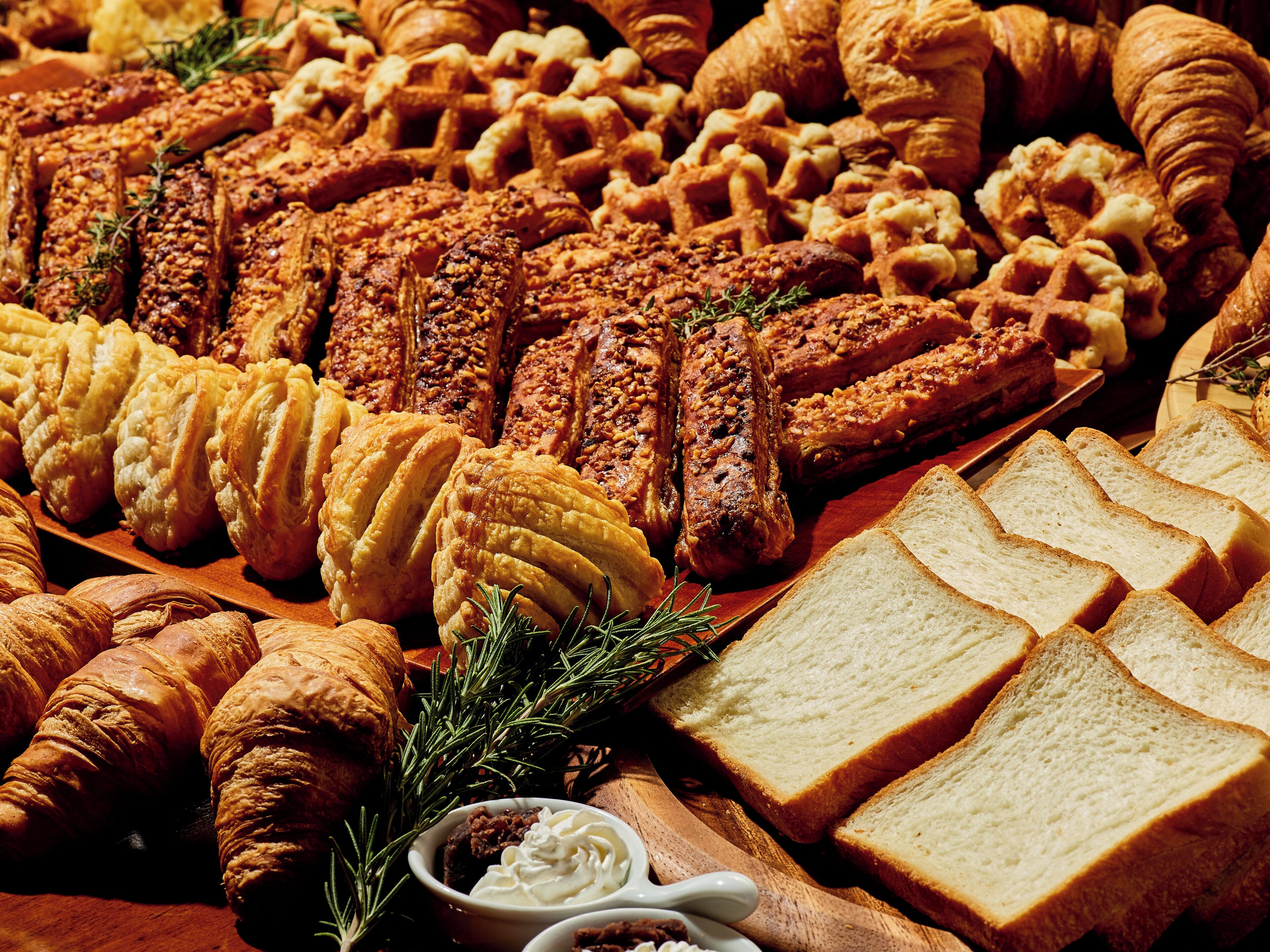 Et udvalg af kager og brød, herunder croissanter, vafler og udskåret brød.
