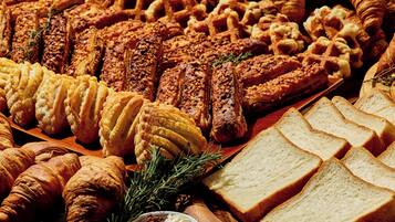 Variedad de pasteles y pan, incluyendo croissants, gofres y una selección de pan cortado.