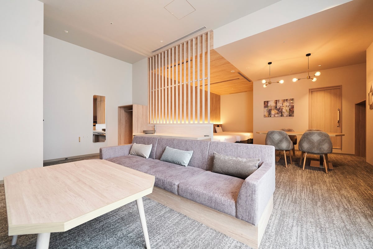 A modern living room with a light-colored sofa, a wooden coffee table, and a dining area with chairs and a table.