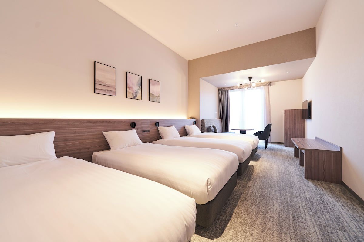 A hotel room with three beds, a desk, a chair, and a TV.