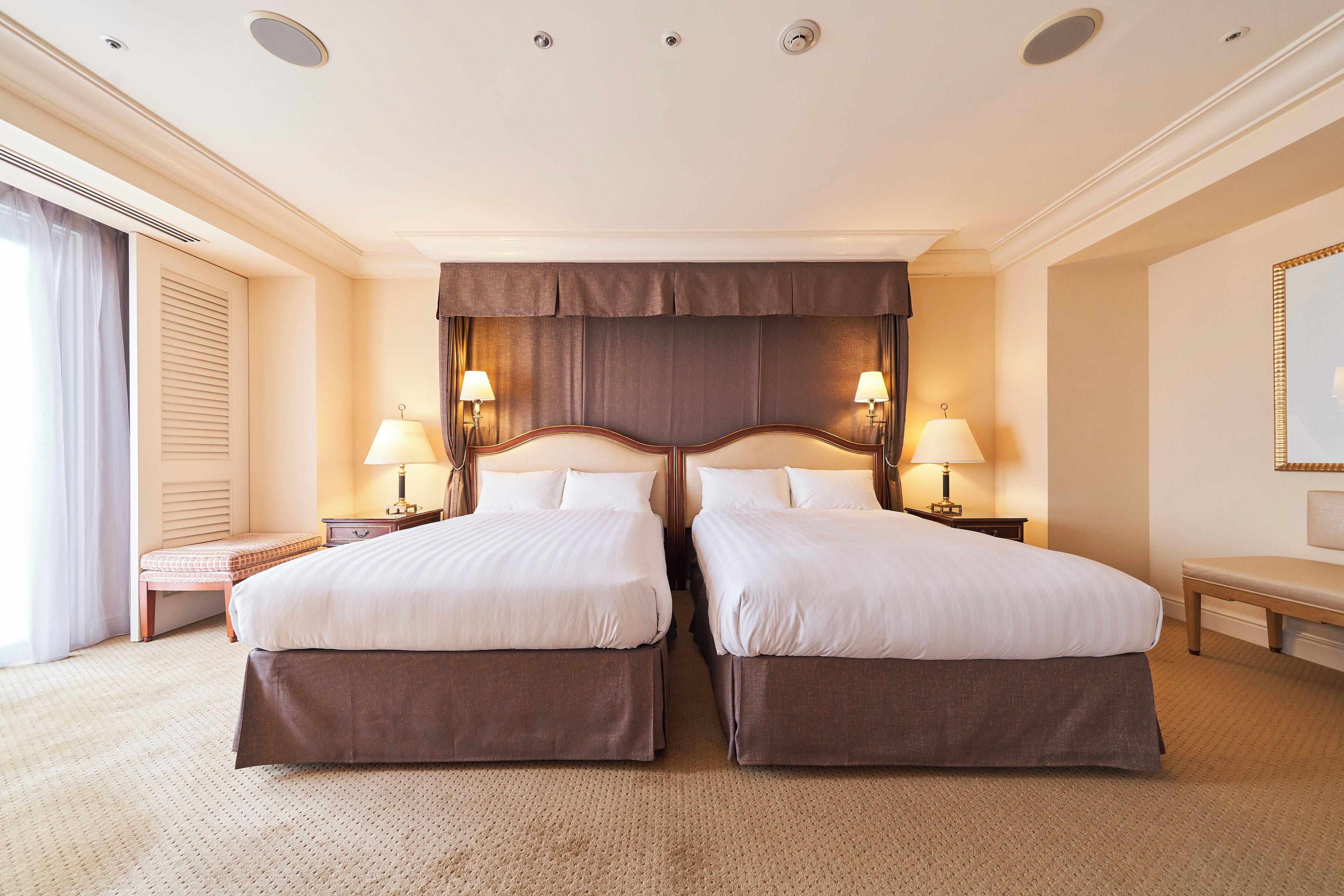 A hotel room with two beds, a large window, and a mirror on the wall.