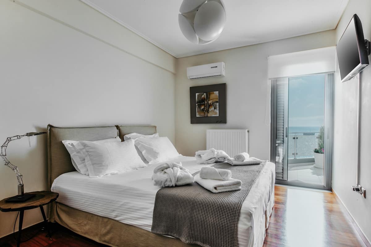 A bedroom with a bed, a desk, a lamp, a TV, and a view of the outside.
