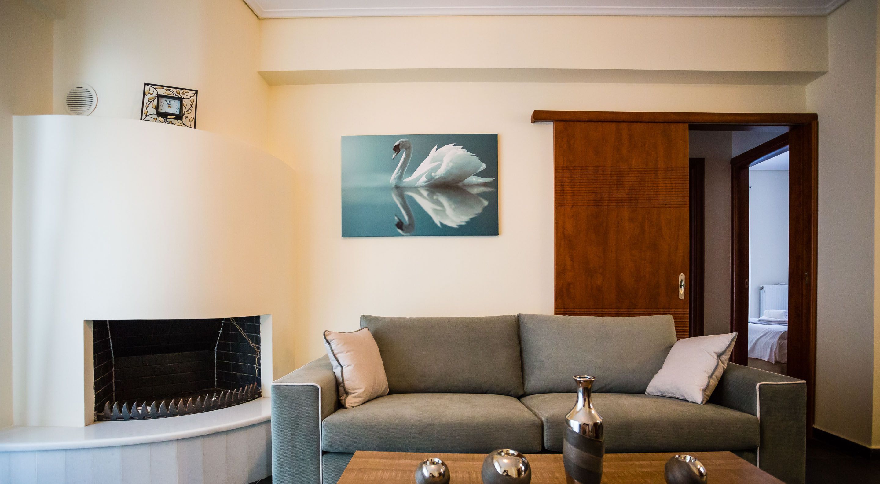 A living room with a grey sofa, a fireplace, and a painting of a swan.