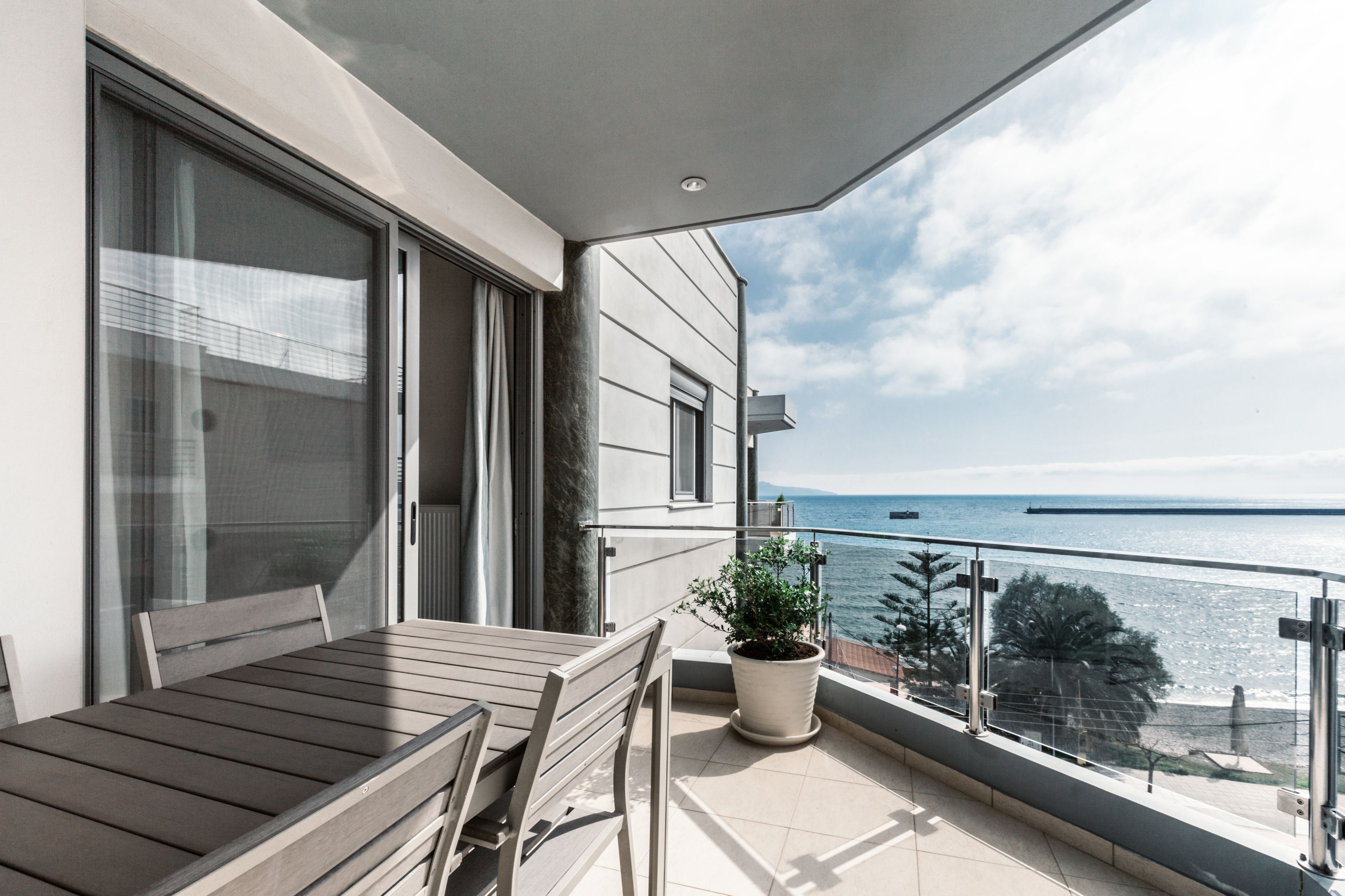 A balcony with a table and chairs, a potted plant, and a view of the sea.